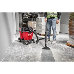 A worker uses the Milwaukee M18 FUEL 9 Gallon Dual-Battery Wet/Dry Vacuum to clean a construction site floor.