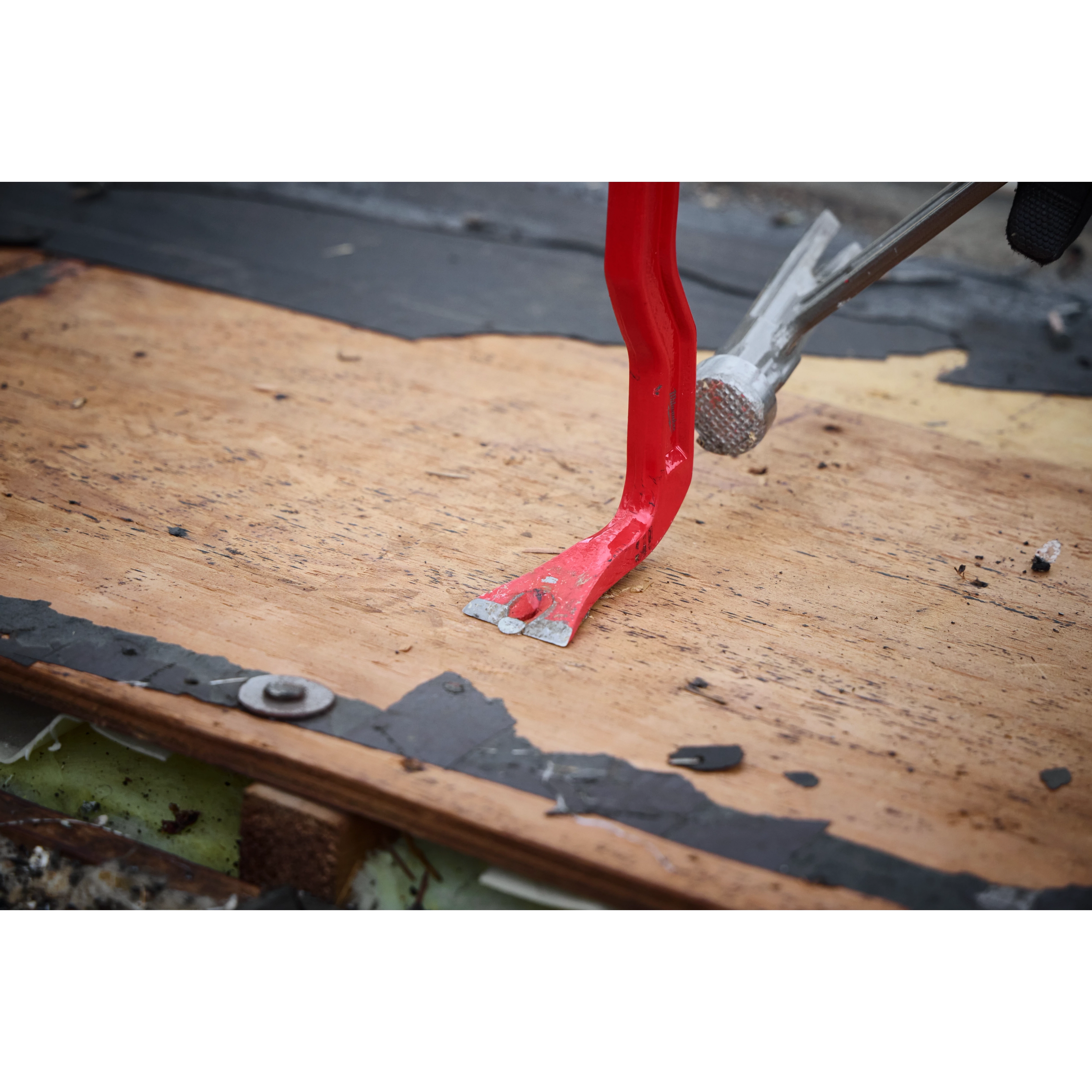 A red 18" Wrecking Bar is prying wood from a surface, showcasing its claw tip's leverage and grip. The bar is being used to remove nails or separate materials, demonstrating its effectiveness in demolition and renovation tasks. Nearby, another tool applies pressure to aid the prying process.