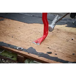 A red 18" Wrecking Bar is prying wood from a surface, showcasing its claw tip's leverage and grip. The bar is being used to remove nails or separate materials, demonstrating its effectiveness in demolition and renovation tasks. Nearby, another tool applies pressure to aid the prying process.