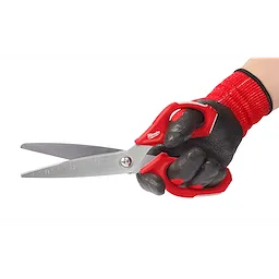 A hand wearing a red and black work glove holds the Offset Jobsite Scissors, which have a red handle and stainless steel blades. The scissors feature measurement markings along one blade.