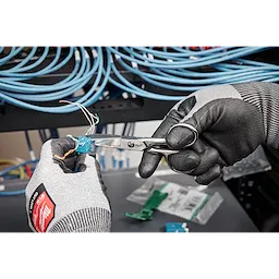 Hands wearing black gloves use Electrician Scissors to cut wires from a blue cable. Coiled blue cables are visible in the background.