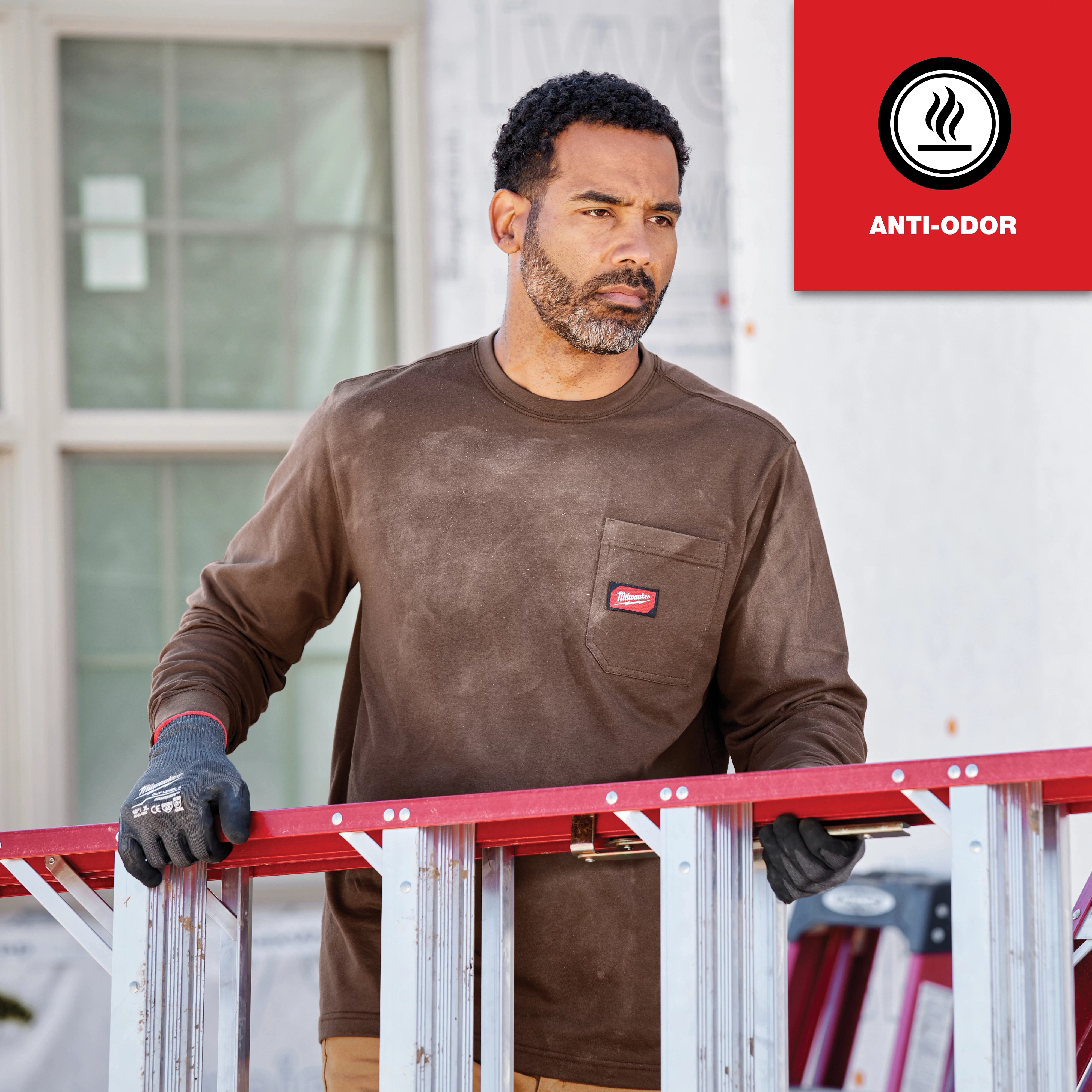Person wearing a GRIDIRON Pocket T-Shirt - Long Sleeve Anti-Odor stands outdoors, holding a red and silver ladder.