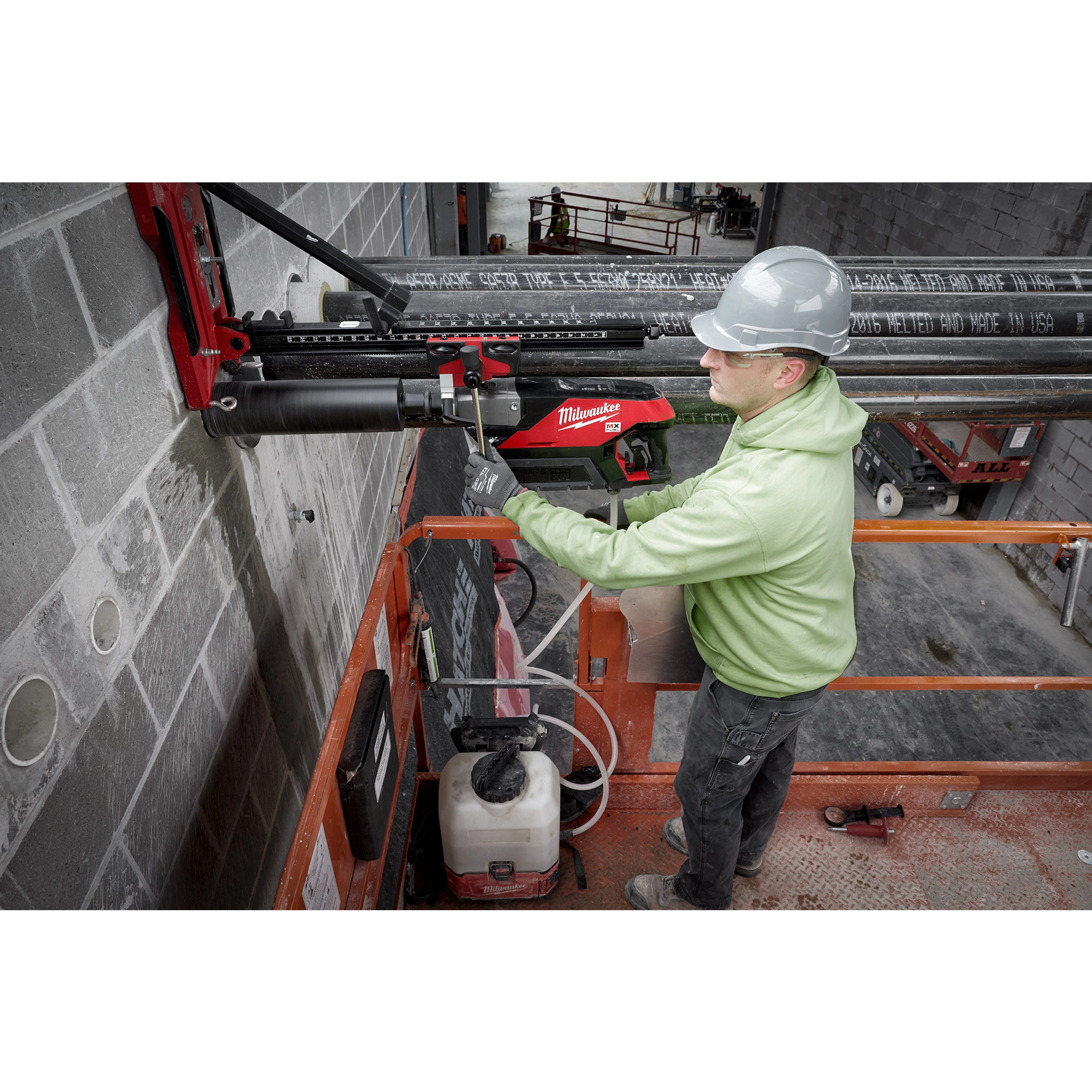 Worker operating the MX FUEL Handheld Core Drill next to a concrete wall while standing on an elevated orange platform.