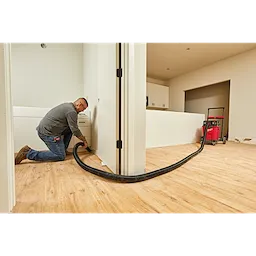 Man using a 2-1/2” x 16' Flexible Hose connected to a red vacuum cleaner to clean or renovate the interior of a house.