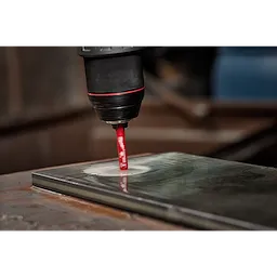 A 1/4" Diamond Grit Hole Saw attached to a drill is cutting a hole into a metallic surface in this close-up image.