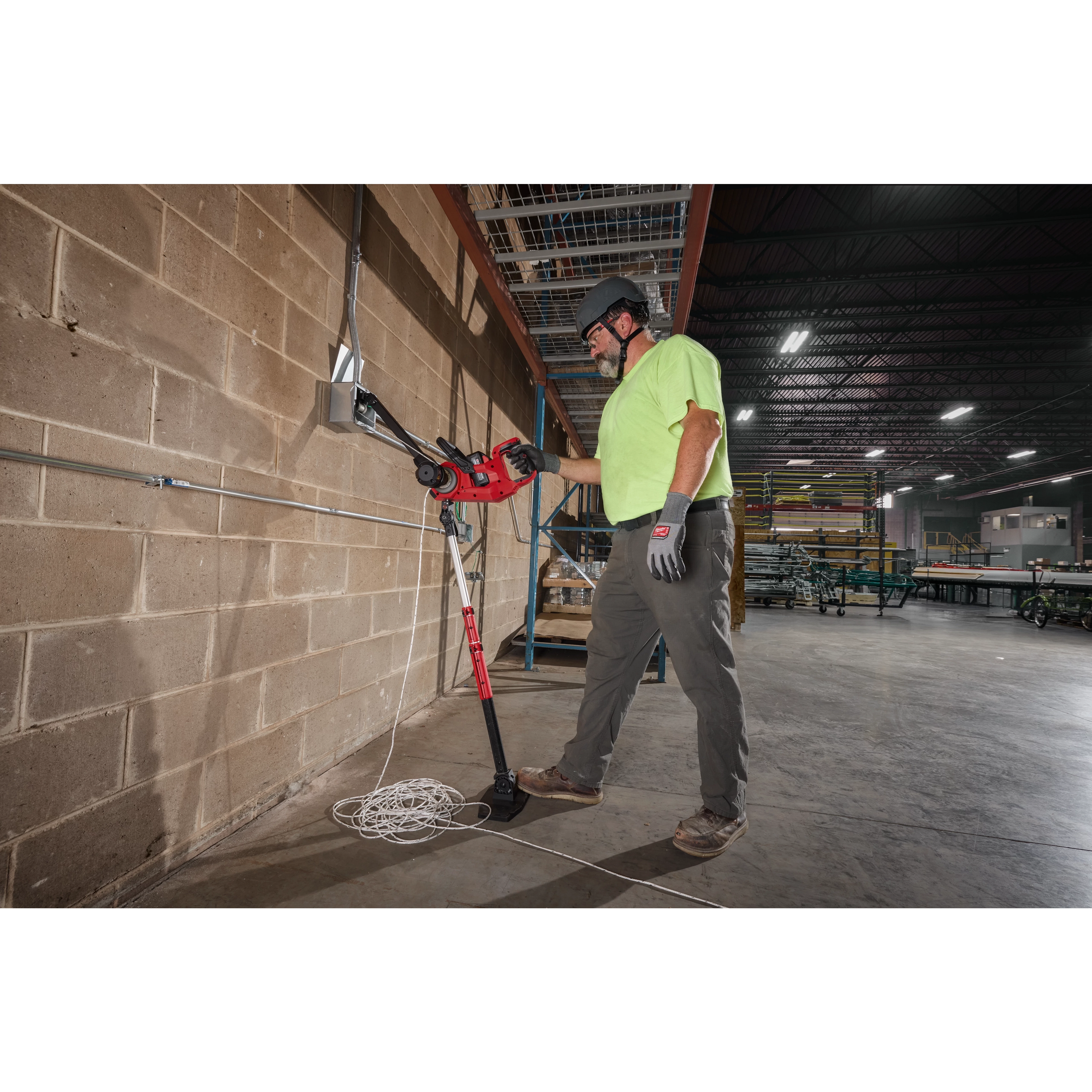 Worker operating an M18 FUEL 1K Wire Puller against a block wall with rope on the floor.