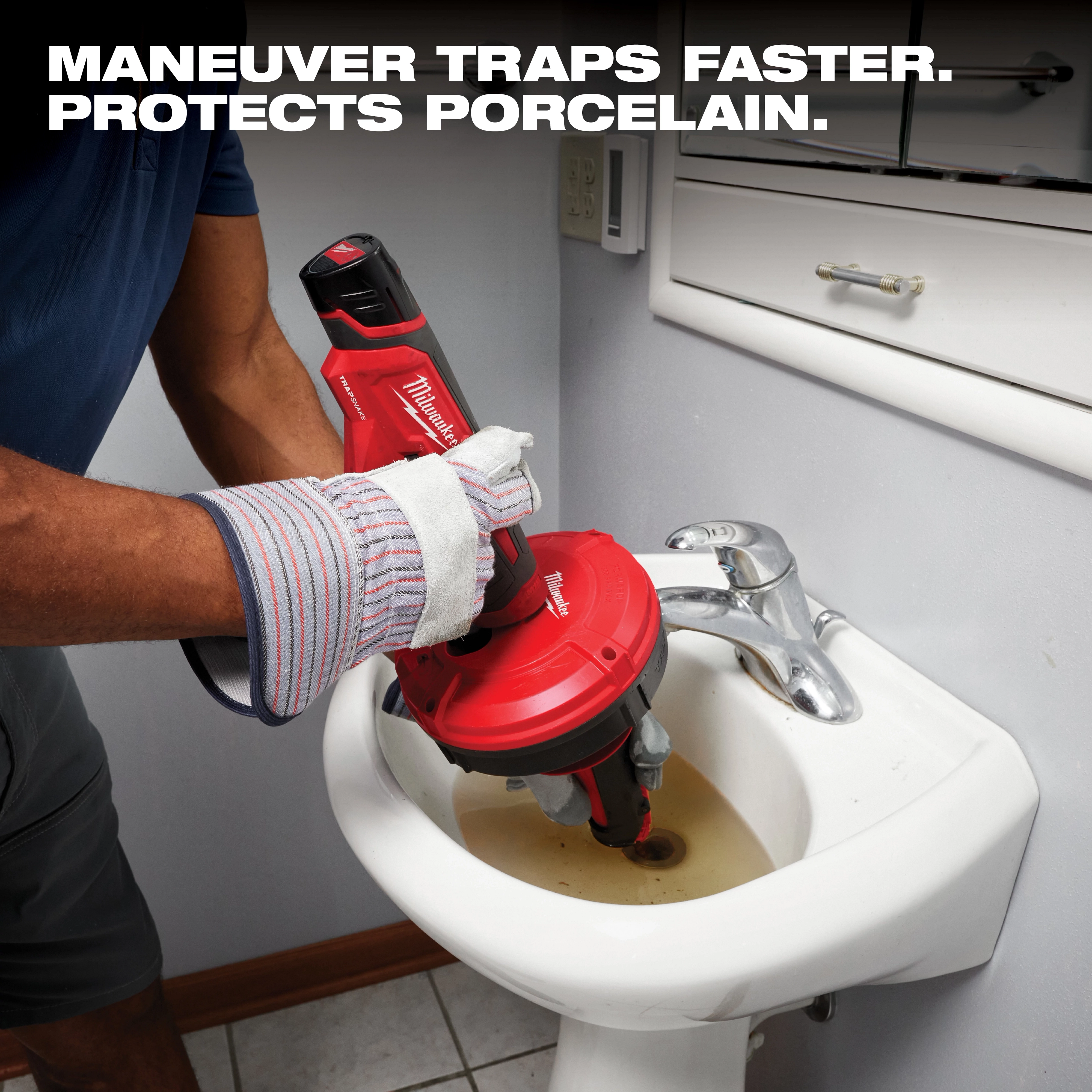 A person wearing work gloves uses a Milwaukee drain cleaning machine on a clogged sink. The tool is red and black with a motorized spool to clear drains. The text above reads, "MANEUVER TRAPS FASTER. PROTECTS PORCELAIN." The sink contains dirty water and the bathroom appears clean and well-maintained.