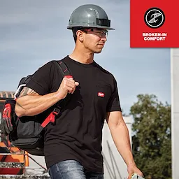 A man wearing a black GRIDIRON Pocket T-Shirt - Short Sleeve with a construction helmet, carrying a tool bag over his shoulder.