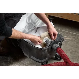A person is installing one of the Fleece Dust Bags (5PK) into a vacuum cleaner. The vacuum has a red and black hose attached, and the person's hands are placing the bag into the compartment.
