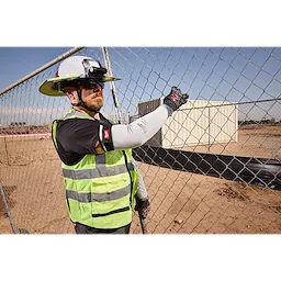 Worker wearing Cut Level 4 Protective Sleeves and high-visibility vest, handling a chain-link fence at a construction site.