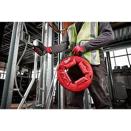 Worker holding a red 1/8" 120' Steel Fish Tape, threading it through metal electrical conduit in a construction setting.