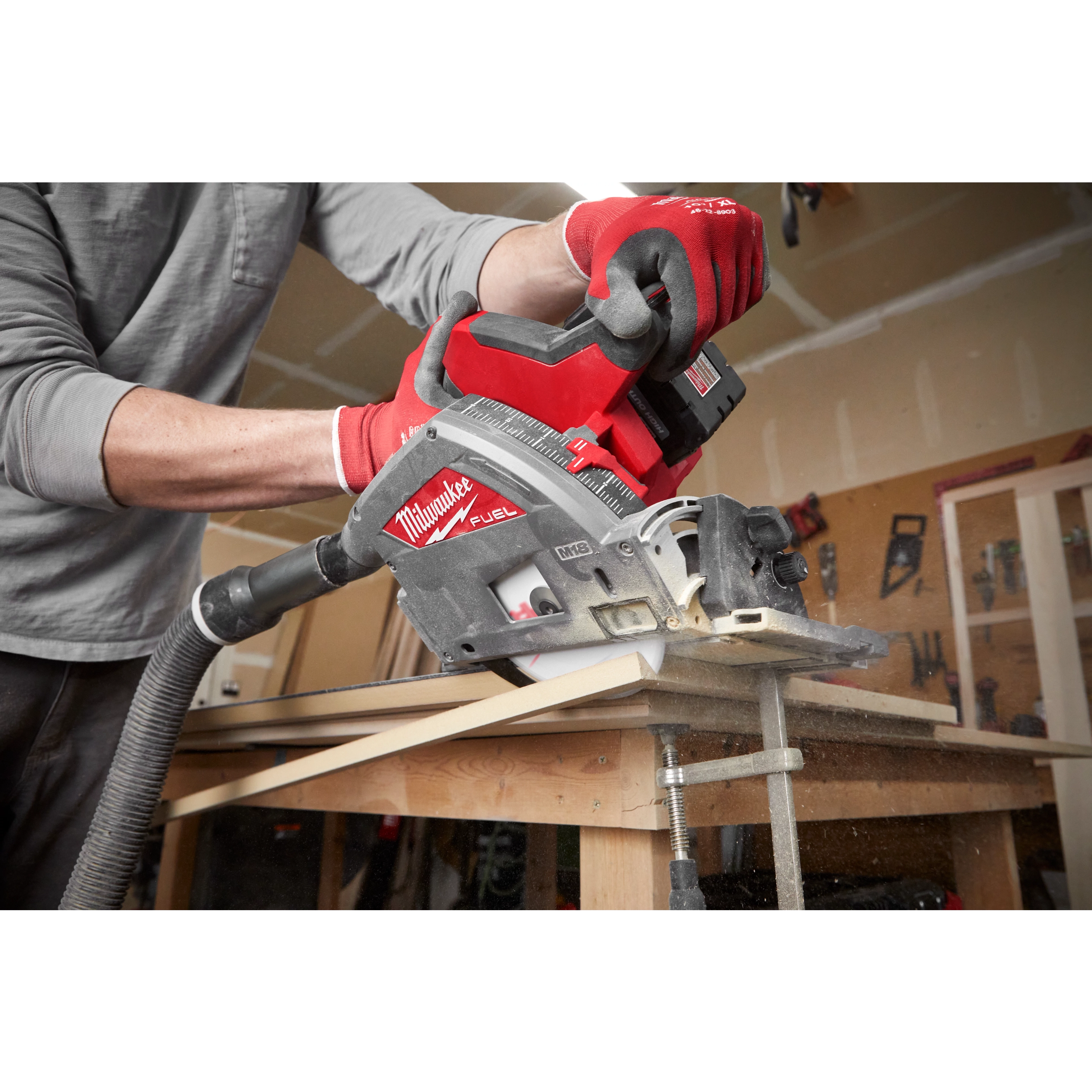 A person is using a Milwaukee M18 FUEL 6 1/2" Plunge Track Saw on a piece of wood in a workshop, creating sawdust.