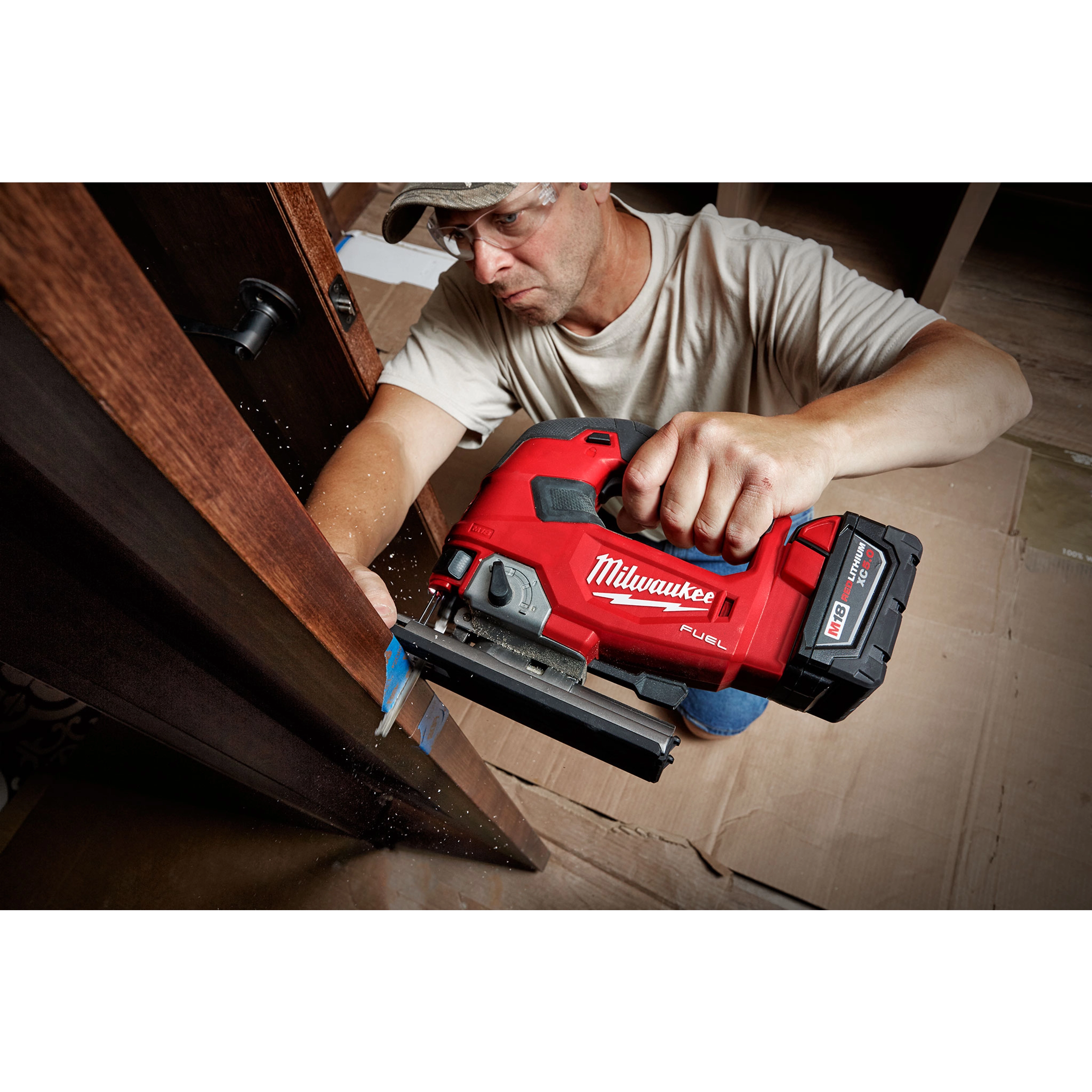 A person is using an M18 FUEL Jigsaw, D-Handle to cut through a wooden surface. The tool is red with a black base.