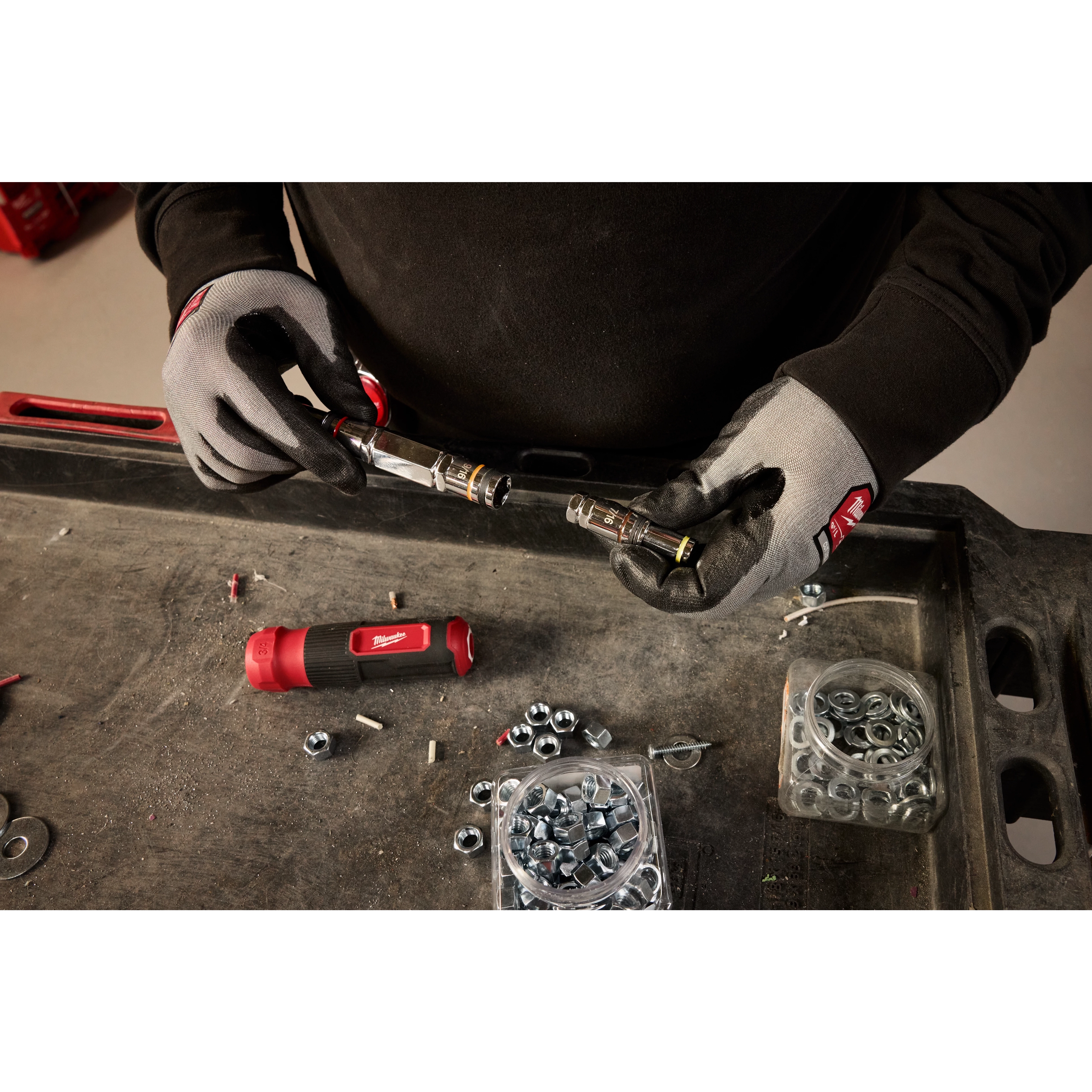 Person wearing protective gloves working with the 7-IN-1 HOLLOWCORE Multi-Nut Driver on a workbench with nuts, bolts, and components.