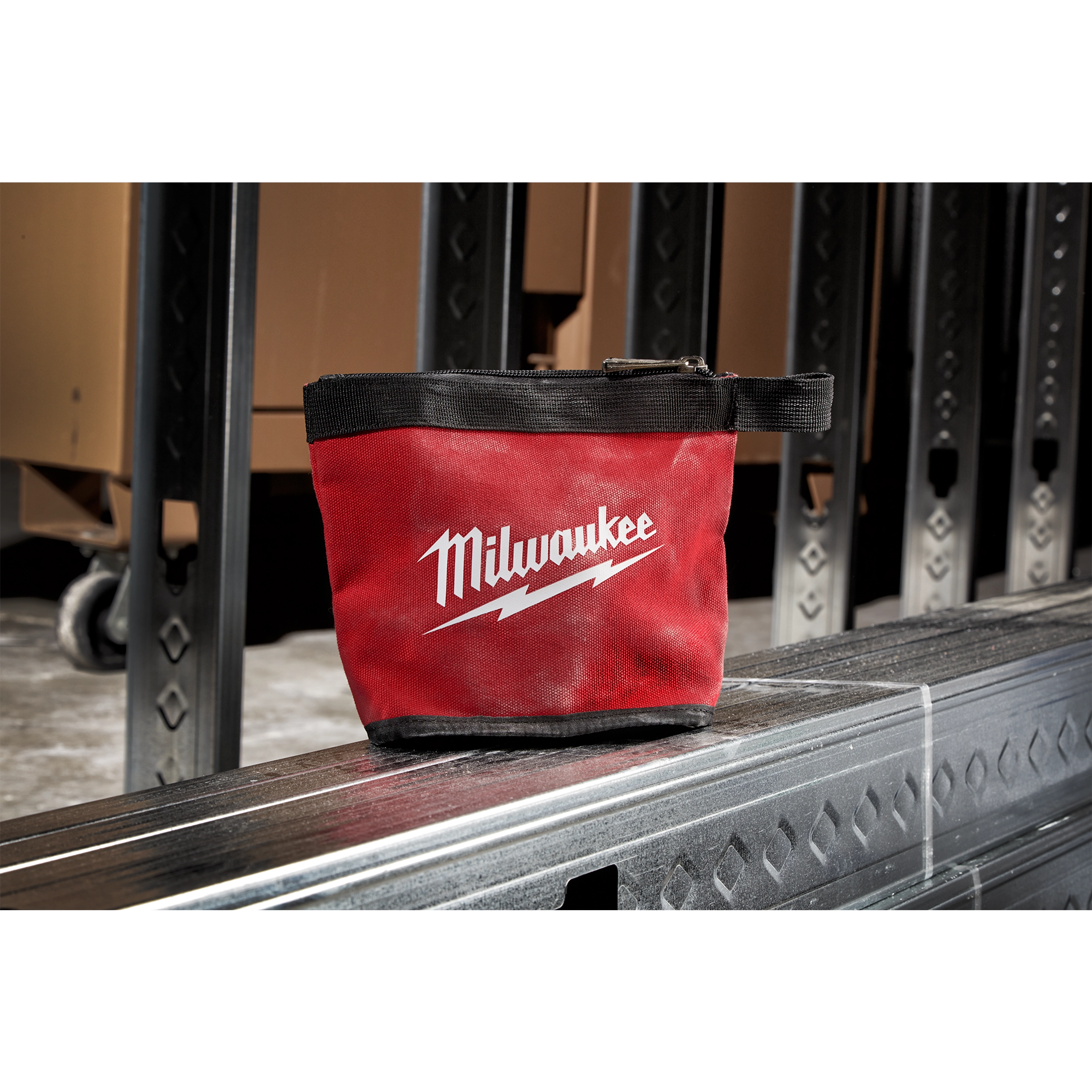 Red and black Zipper Pouch with the brand name Milwaukee and a lightning bolt logo, placed on a metal surface in an industrial setting.