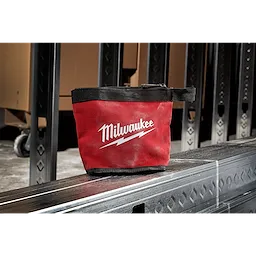 Red and black Zipper Pouch with the brand name Milwaukee and a lightning bolt logo, placed on a metal surface in an industrial setting.