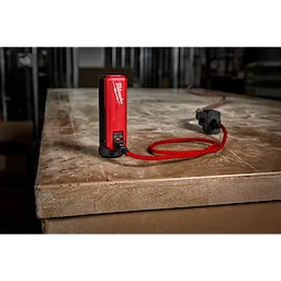 The REDLITHIUM™ USB Charger and Portable Power Source Kit is placed on a dusty wooden surface. It features a red and black charger connected to a red USB cable, highlighting its portable design suitable for various work environments.