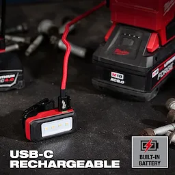 Milwaukee USB-C rechargeable work light with built-in battery on a workbench near tools and bolts.