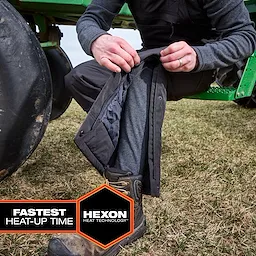 Person unzipping pants leg to reveal Milwaukee Heated Merino Wool Baselayer Pants beside farm equipment.