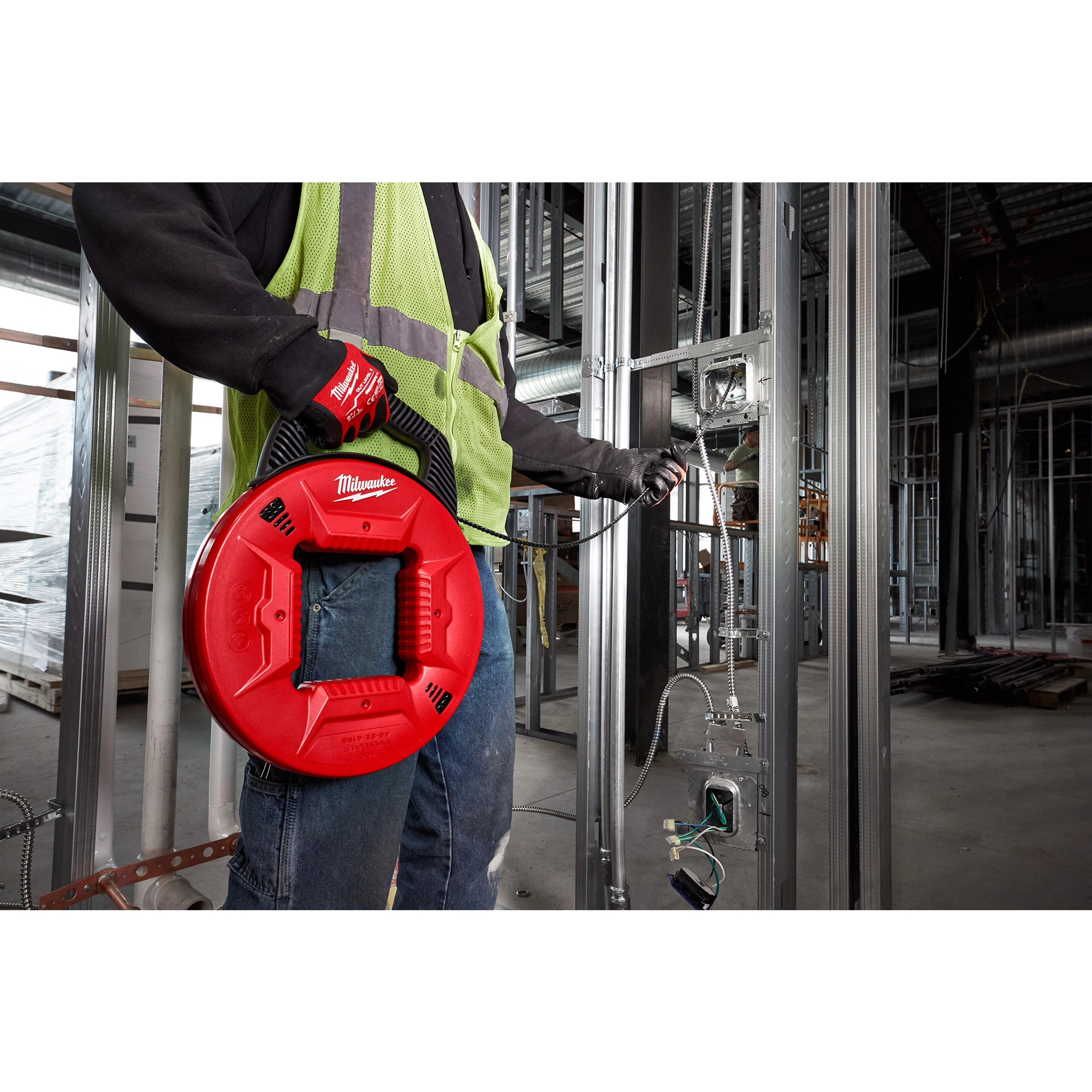 Person holding 100% Polyester Fish Tape with Flexible Leader, a red and black tool, being used in a construction site.