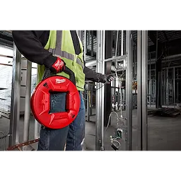 Person holding 100% Polyester Fish Tape with Flexible Leader, a red and black tool, being used in a construction site.