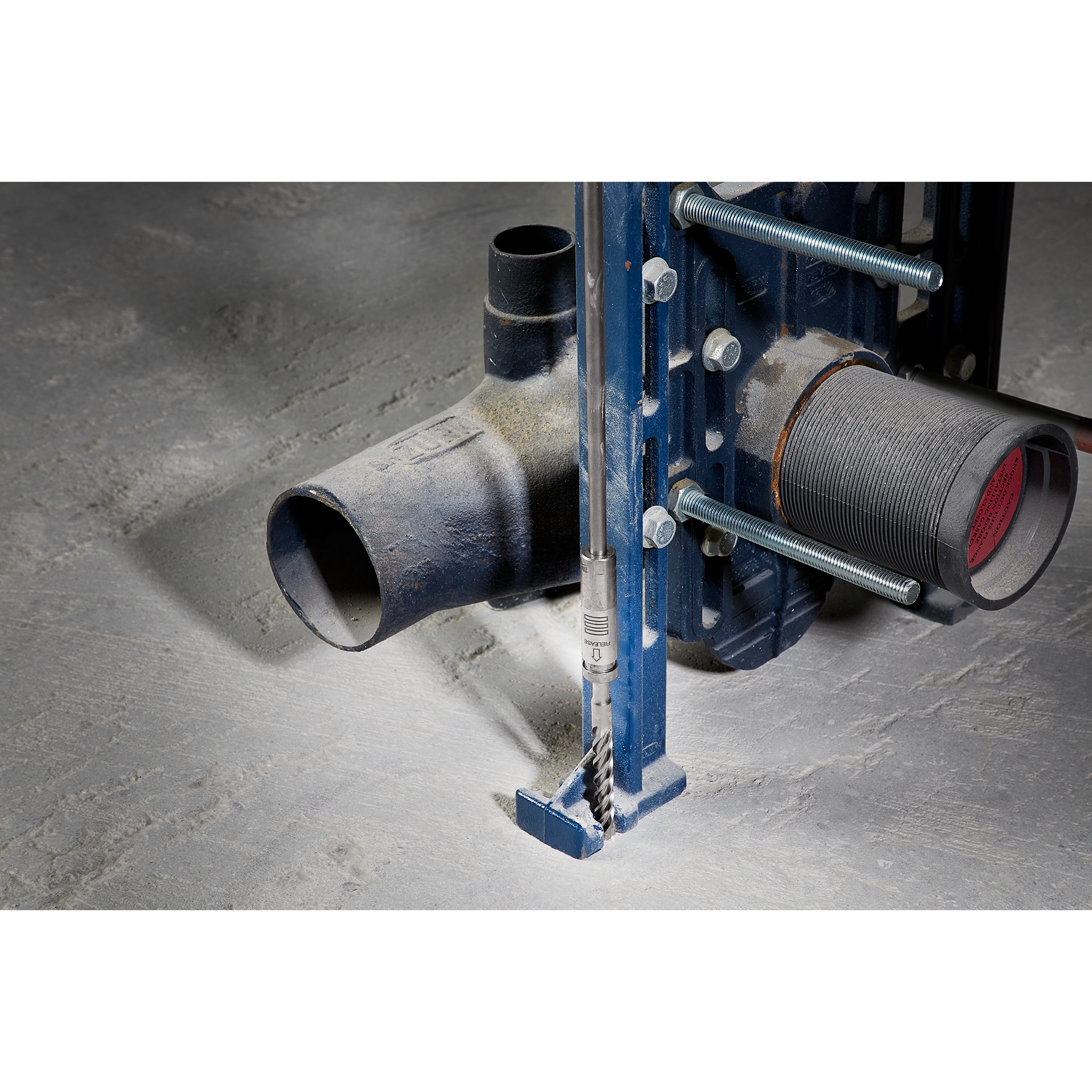 SDS PLUS 18” EXTENSION attached to a blue metal frame, drilling into a concrete floor, next to a black pipe fitting.