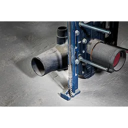 SDS PLUS 18” EXTENSION attached to a blue metal frame, drilling into a concrete floor, next to a black pipe fitting.