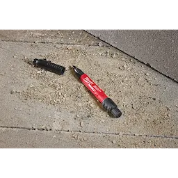 The INKZALL™ Double Sided Black Jobsite Marker – Ultra Fine & Fine Point lies on a rough, concrete surface with its cap removed, exposing the ultra-fine point.