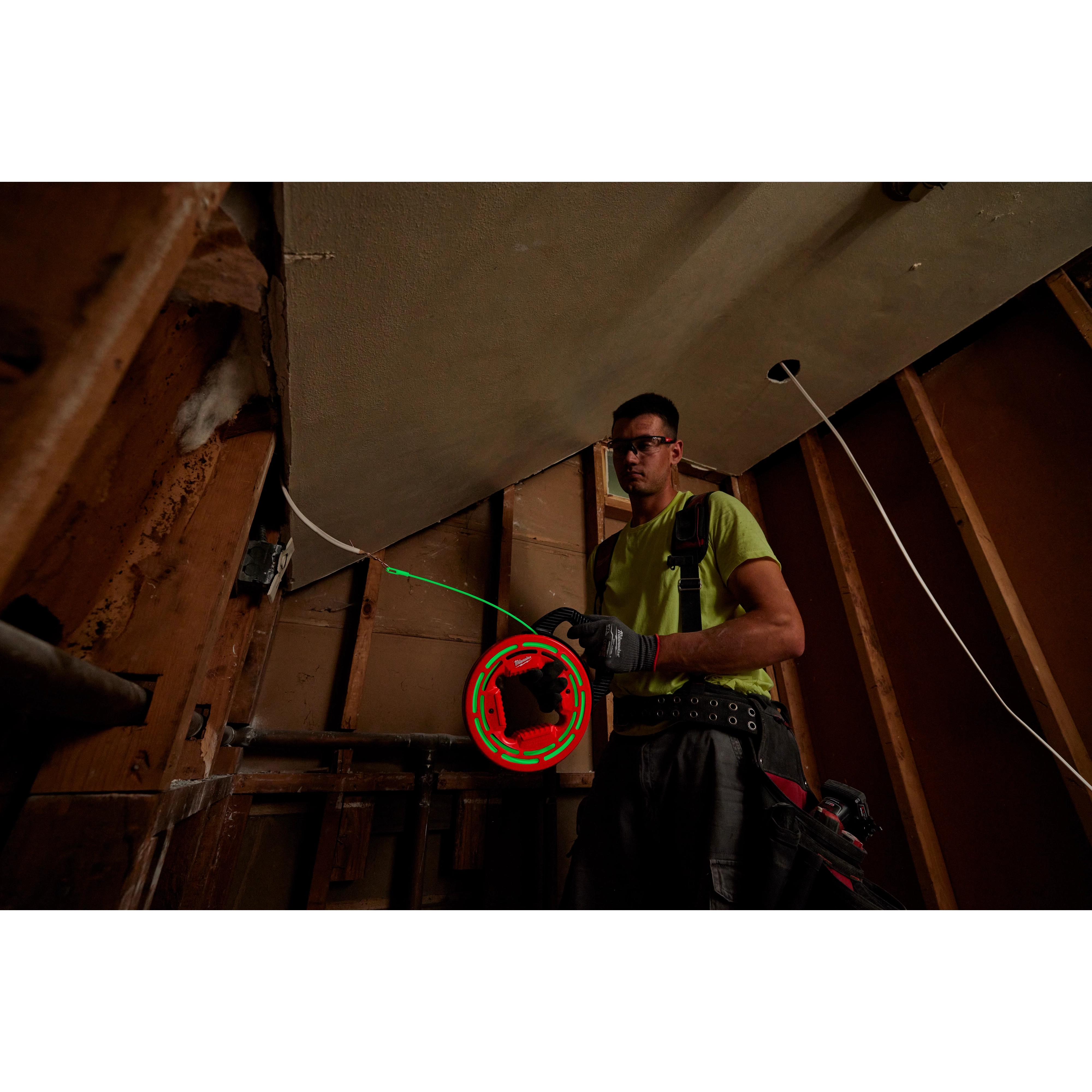 Worker using 40%27 Glow Fish Tape to pull wire through wall framing at a construction site. The tool glows for easy visibility.