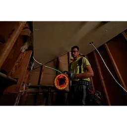 Worker using 40%27 Glow Fish Tape to pull wire through wall framing at a construction site. The tool glows for easy visibility.