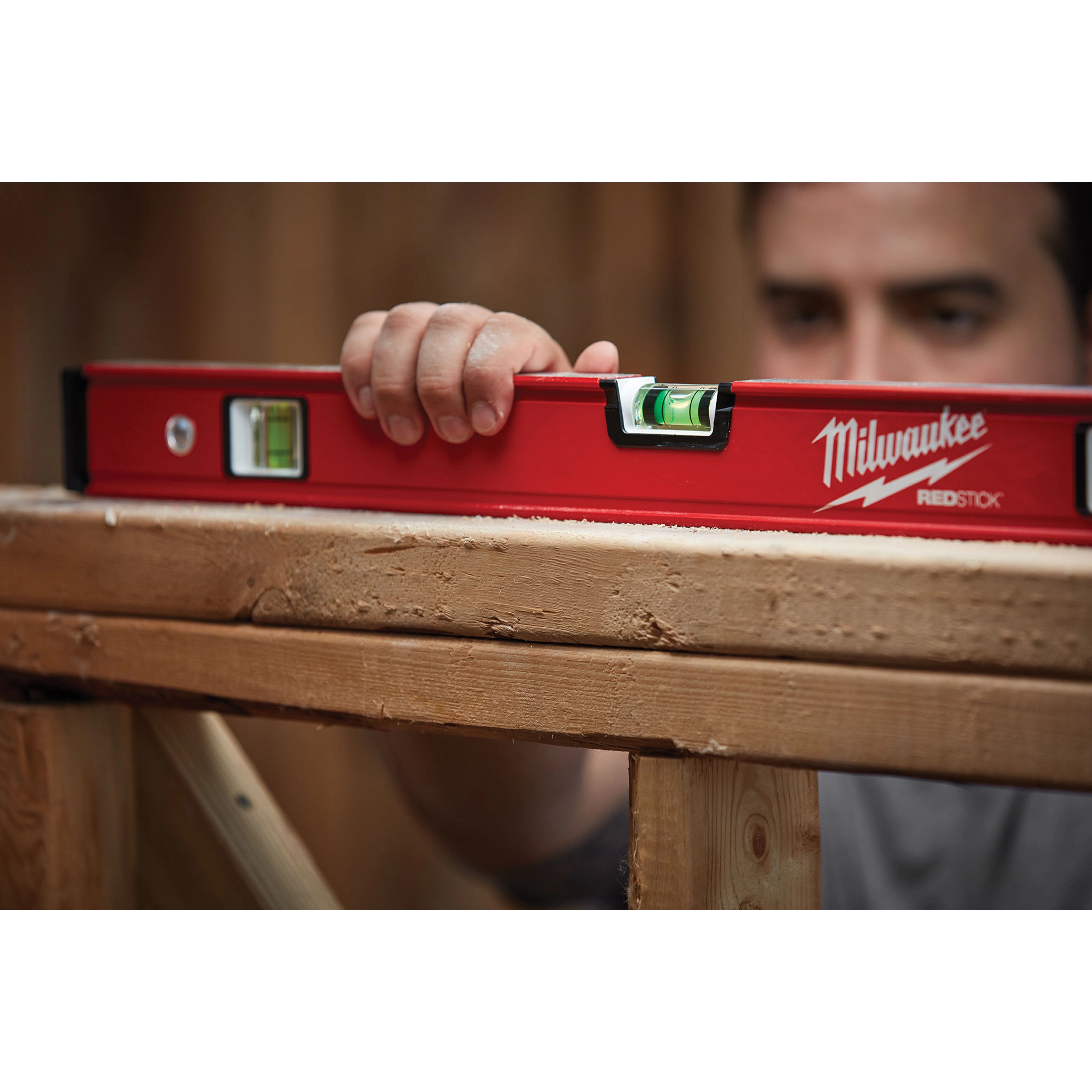 A hand holds a REDSTICK Level on wooden beams, ensuring the beams are perfectly horizontal for construction.