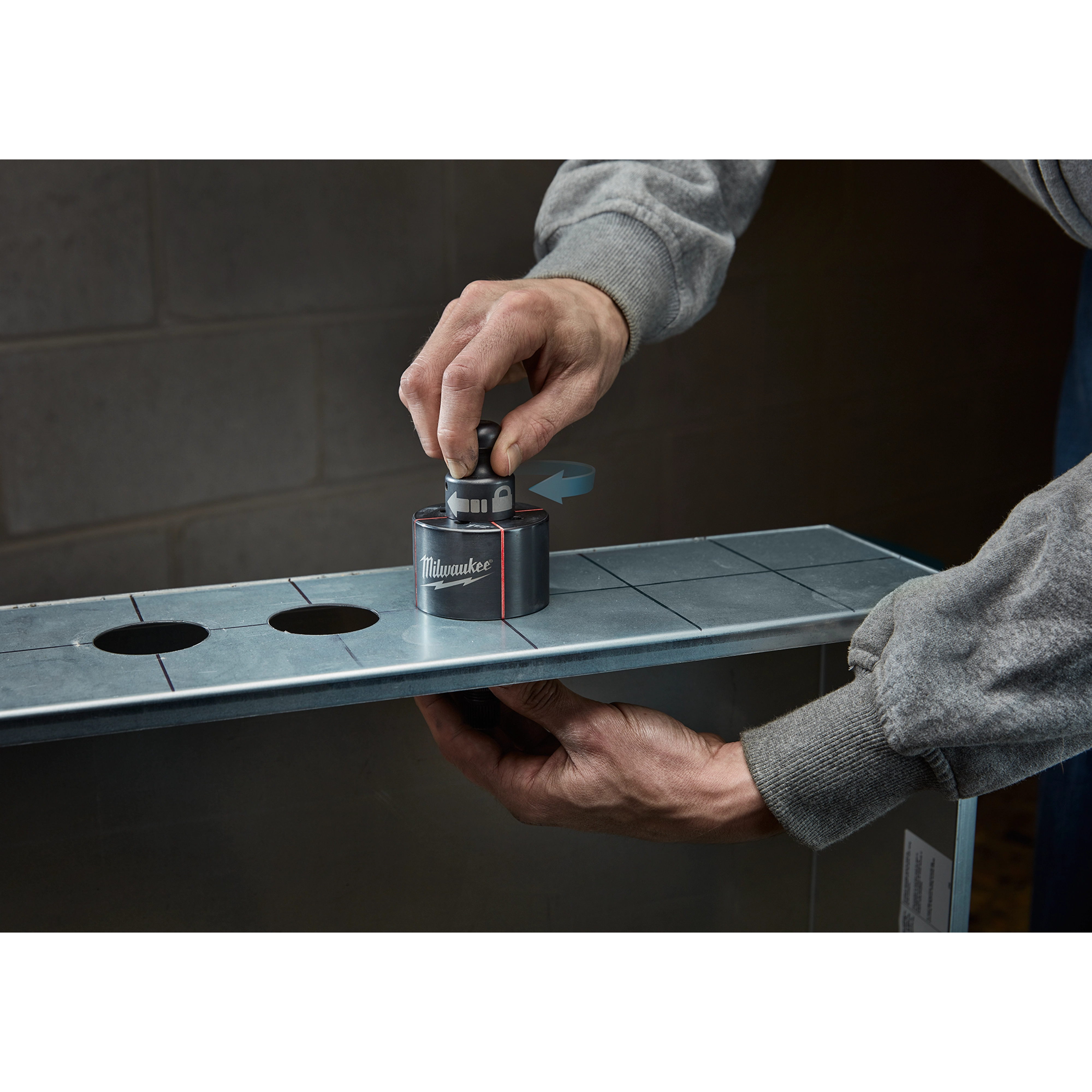 A person uses a Milwaukee Draw Stud tool on a metal sheet with pre-cut holes.