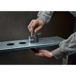 A person uses a Milwaukee Draw Stud tool on a metal sheet with pre-cut holes.