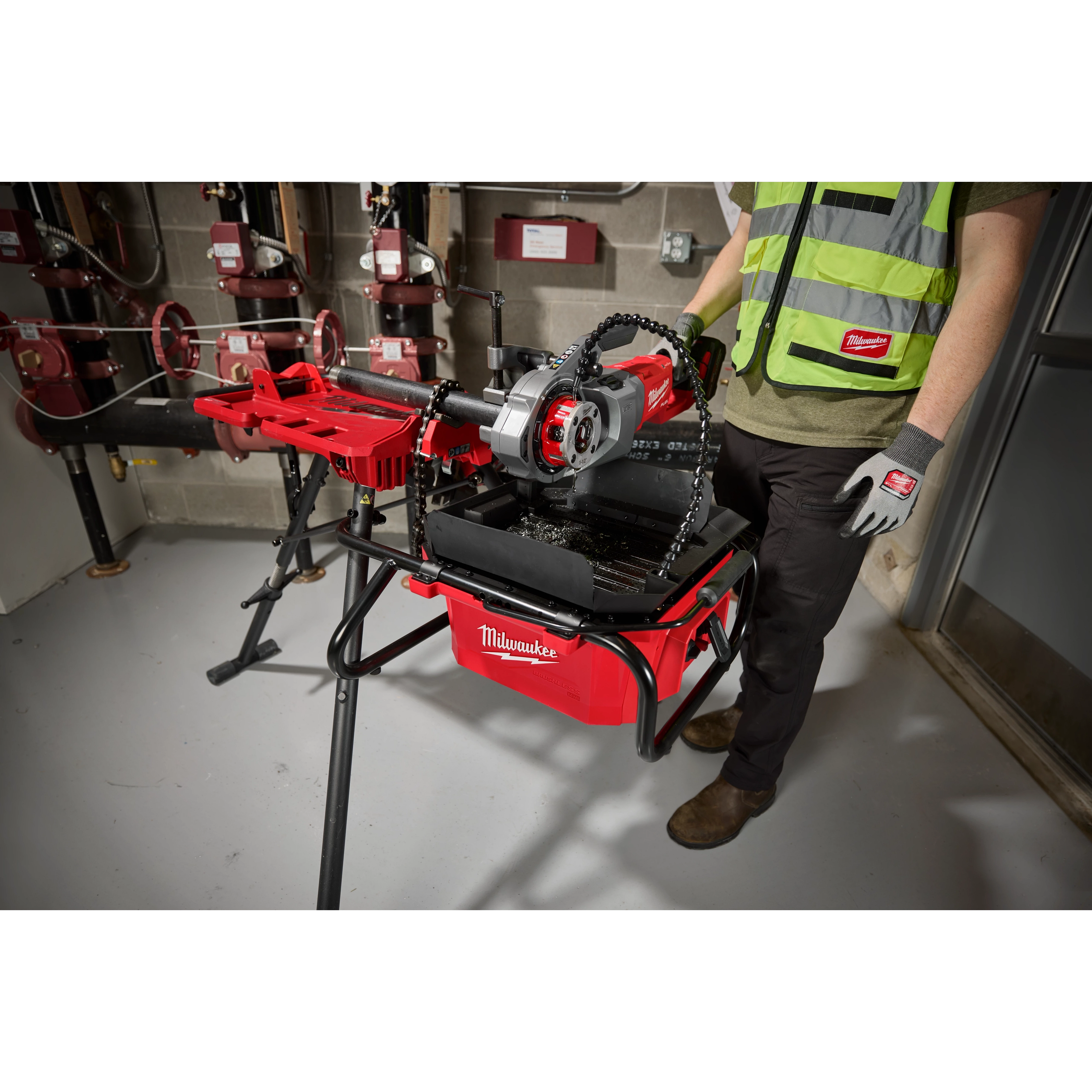 Professional using the M18 Brushless Pipe Threading Oiler in a workshop setting, mounted on a stand with various piping tools.
