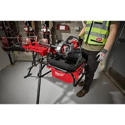 Professional using the M18 Brushless Pipe Threading Oiler in a workshop setting, mounted on a stand with various piping tools.
