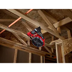 Red and black M18 Jobsite Fan mounted on the wooden frame of a ceiling in a construction site.