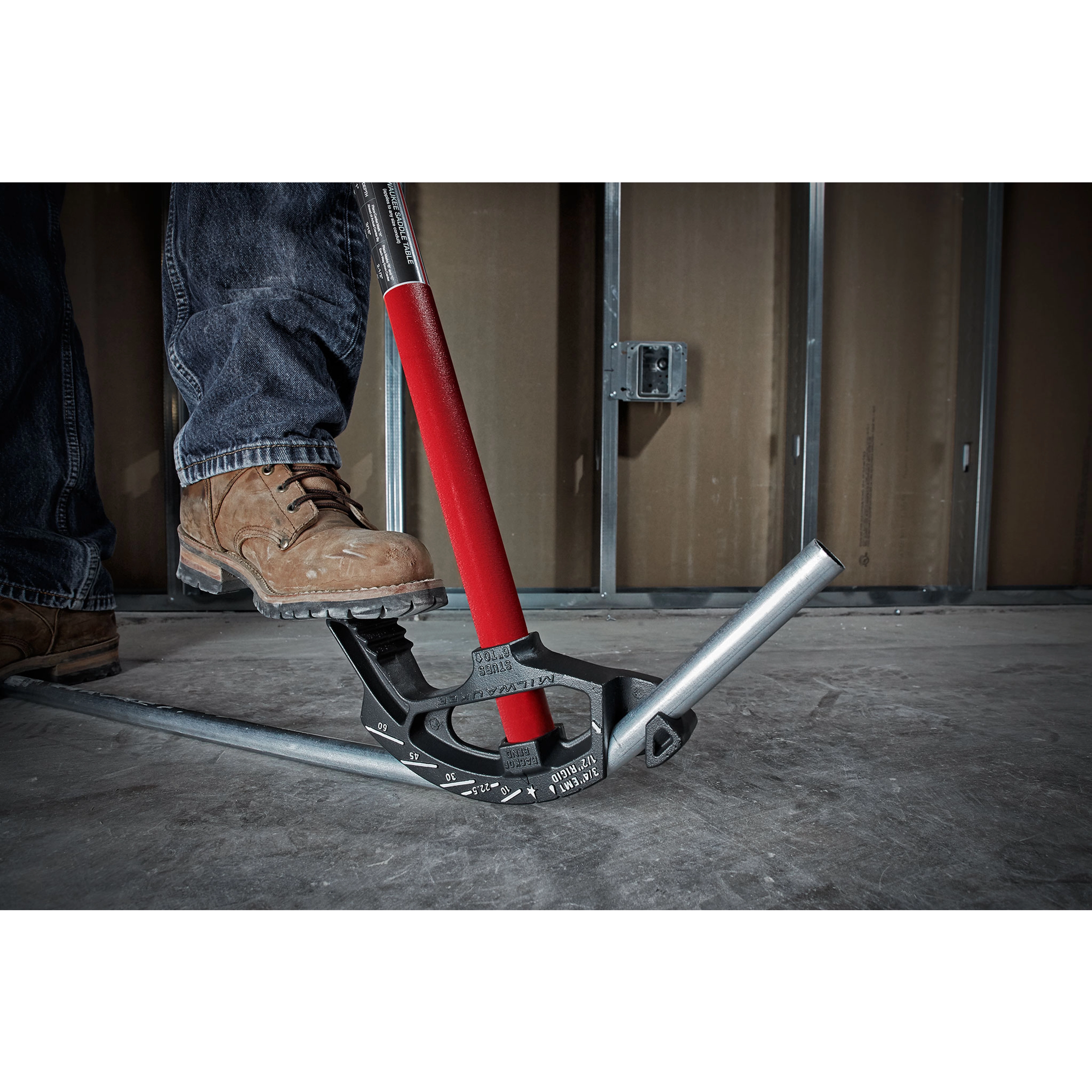 Person using a 3/4" EMT Iron Conduit Bender to bend a metal conduit on a concrete floor. The tool has a red handle.