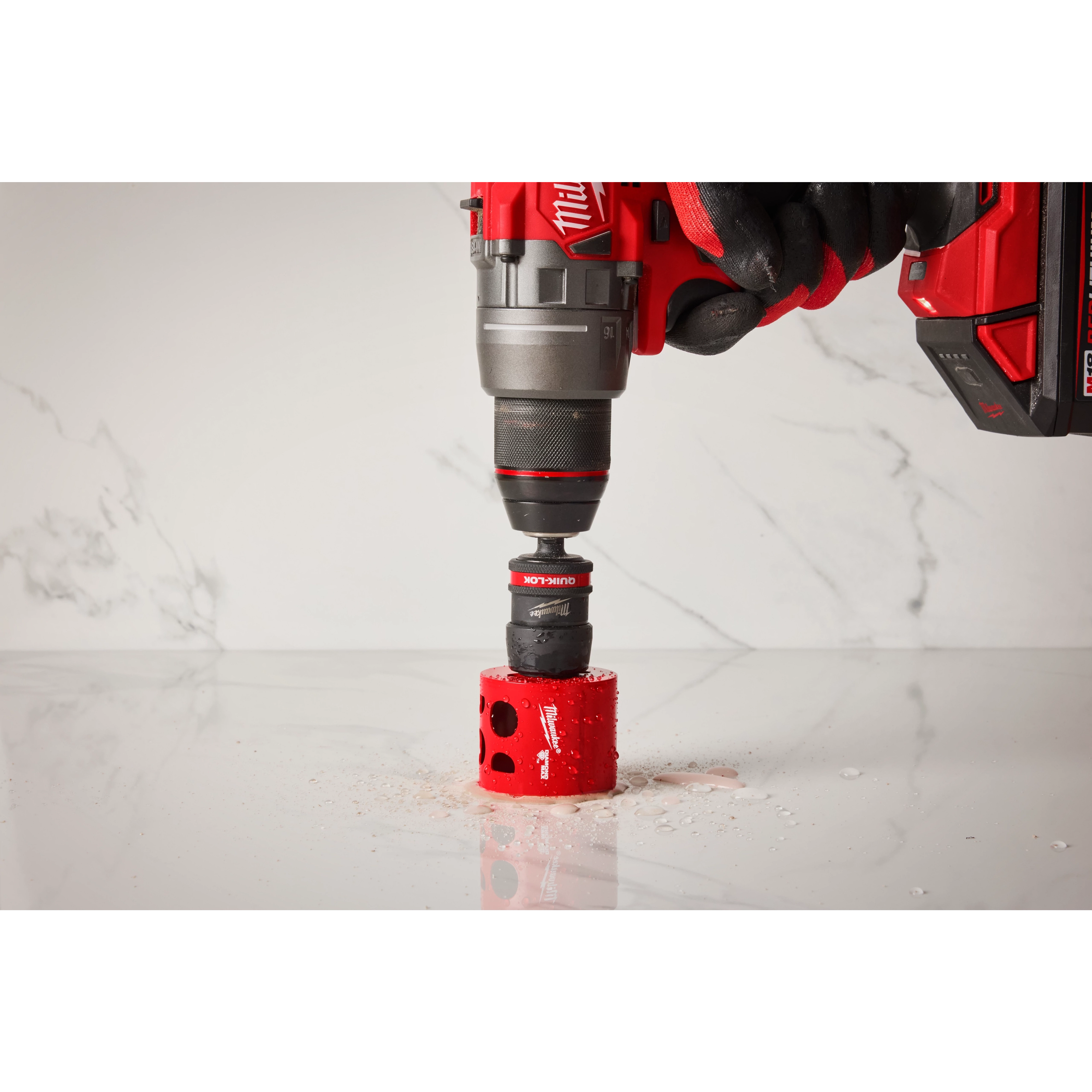 A red and black Milwaukee electric drill with a 2PK Large Thread Pin Adapter for QUIK-LOK™ Arbor attached is drilling into a white marble surface. The drill bit is surrounded by red shavings.