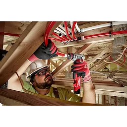 Man wearing gloves using M12 FUEL ProPEX Expander on red PEX pipes in wooden scaffolding.