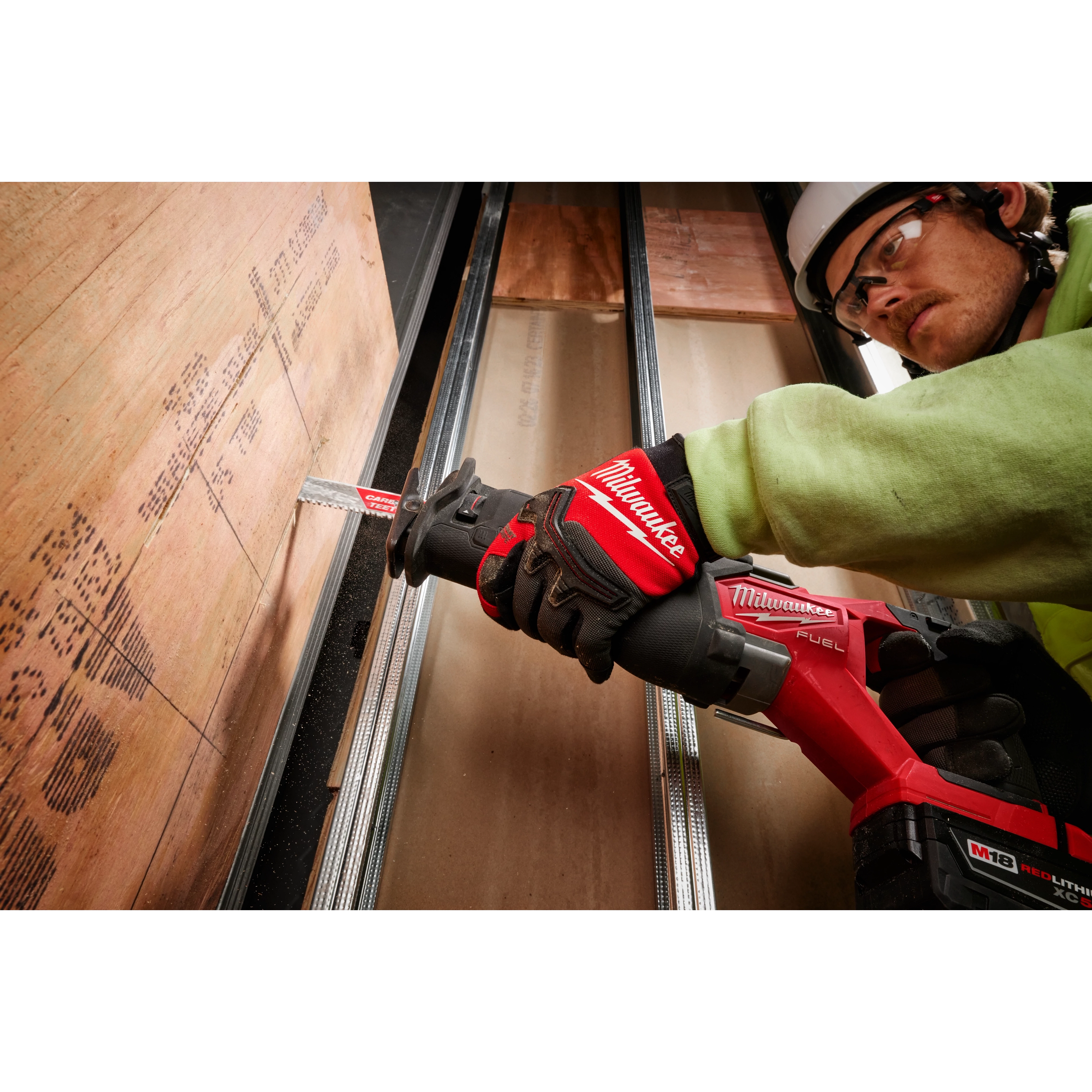 Person wearing Wrecking Work Gloves - L while using a red reciprocating saw to cut a piece of plywood on metal beams.