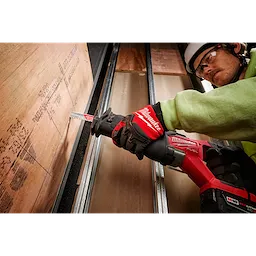 Person wearing Wrecking Work Gloves - L while using a red reciprocating saw to cut a piece of plywood on metal beams.