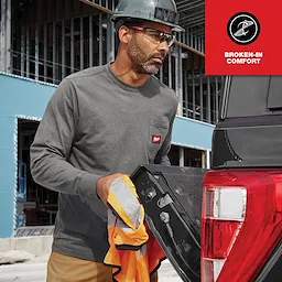 Man wearing the long sleeve GRIDIRON Pocket T-Shirt - Broken-in Comfort. He is holding a neon work jacket by a truck.