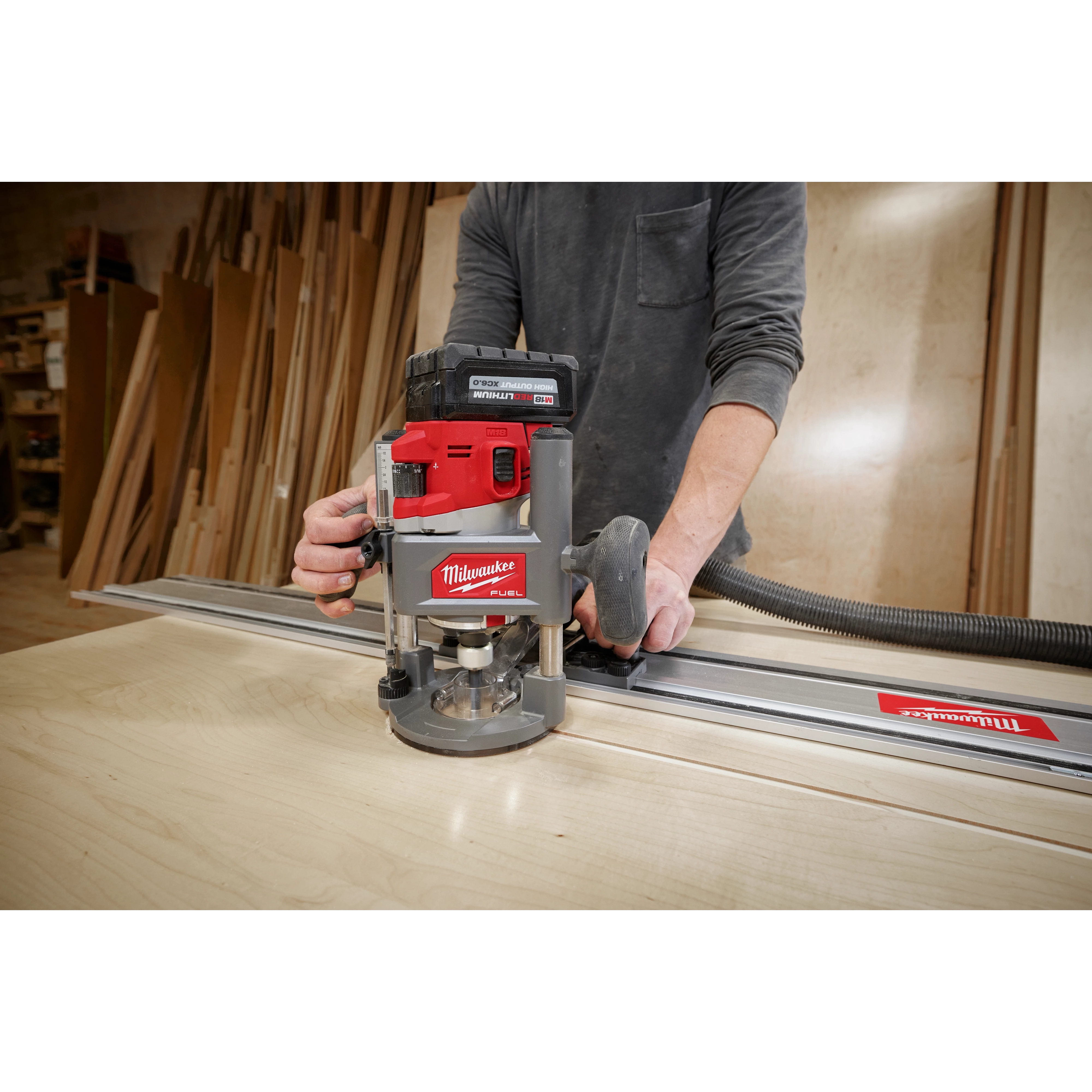 Person using a Milwaukee M18 FUEL 1/2" Router on a wooden board, attached to a guide rail in a workshop setting.