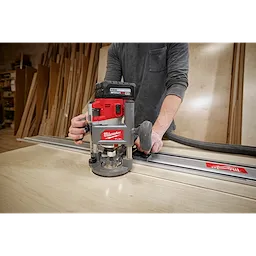Person using a Milwaukee M18 FUEL 1/2" Router on a wooden board, attached to a guide rail in a workshop setting.