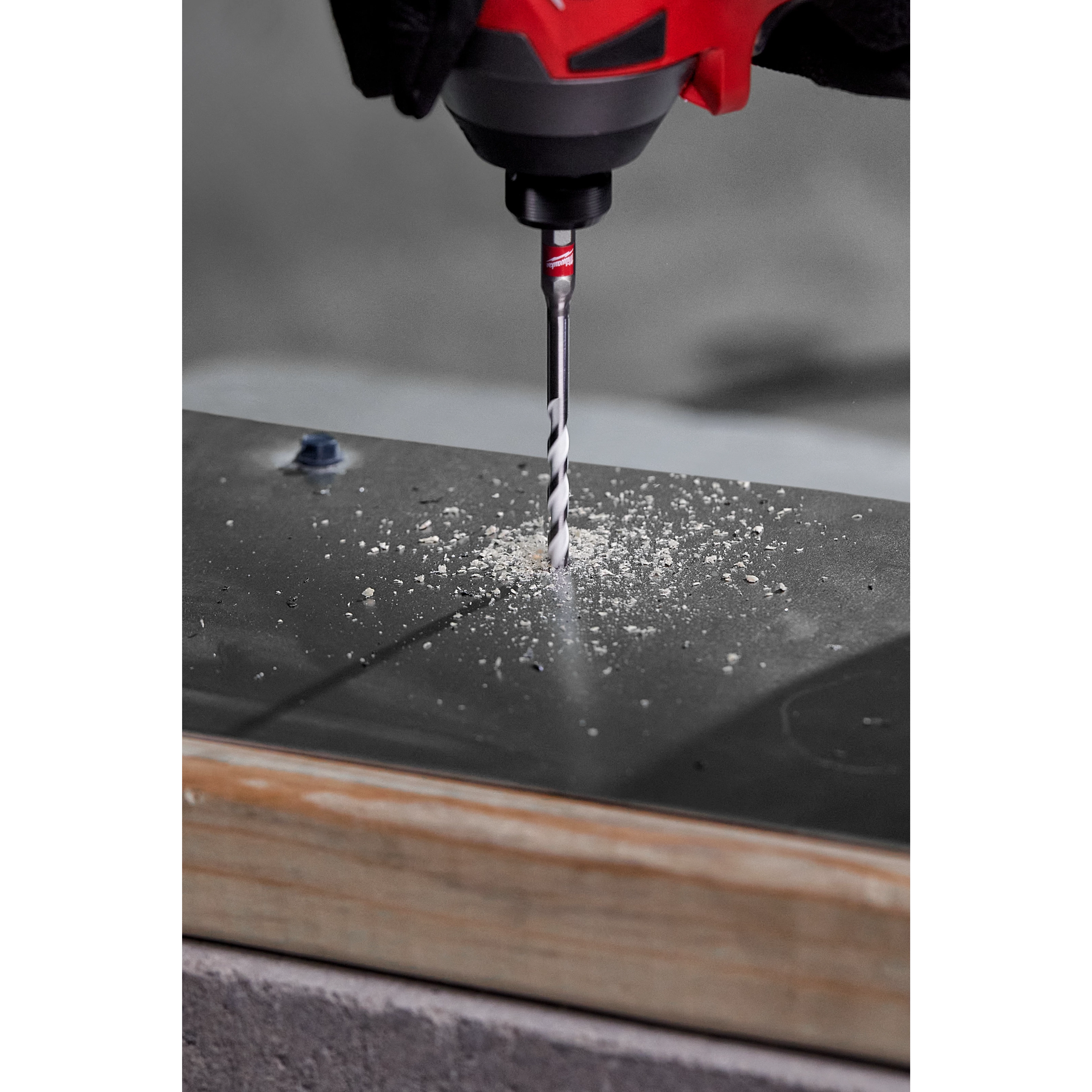 A 1/4" carbide multi-material drill bit is shown drilling through a metal surface, producing shavings, attached to a red power tool.