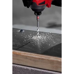 A 1/4" carbide multi-material drill bit is shown drilling through a metal surface, producing shavings, attached to a red power tool.