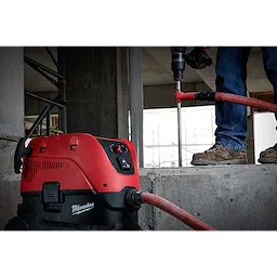 A worker uses an SDS Vacuum Bit attached to a red and black vacuum cleaner to drill into a concrete surface at a construction site.