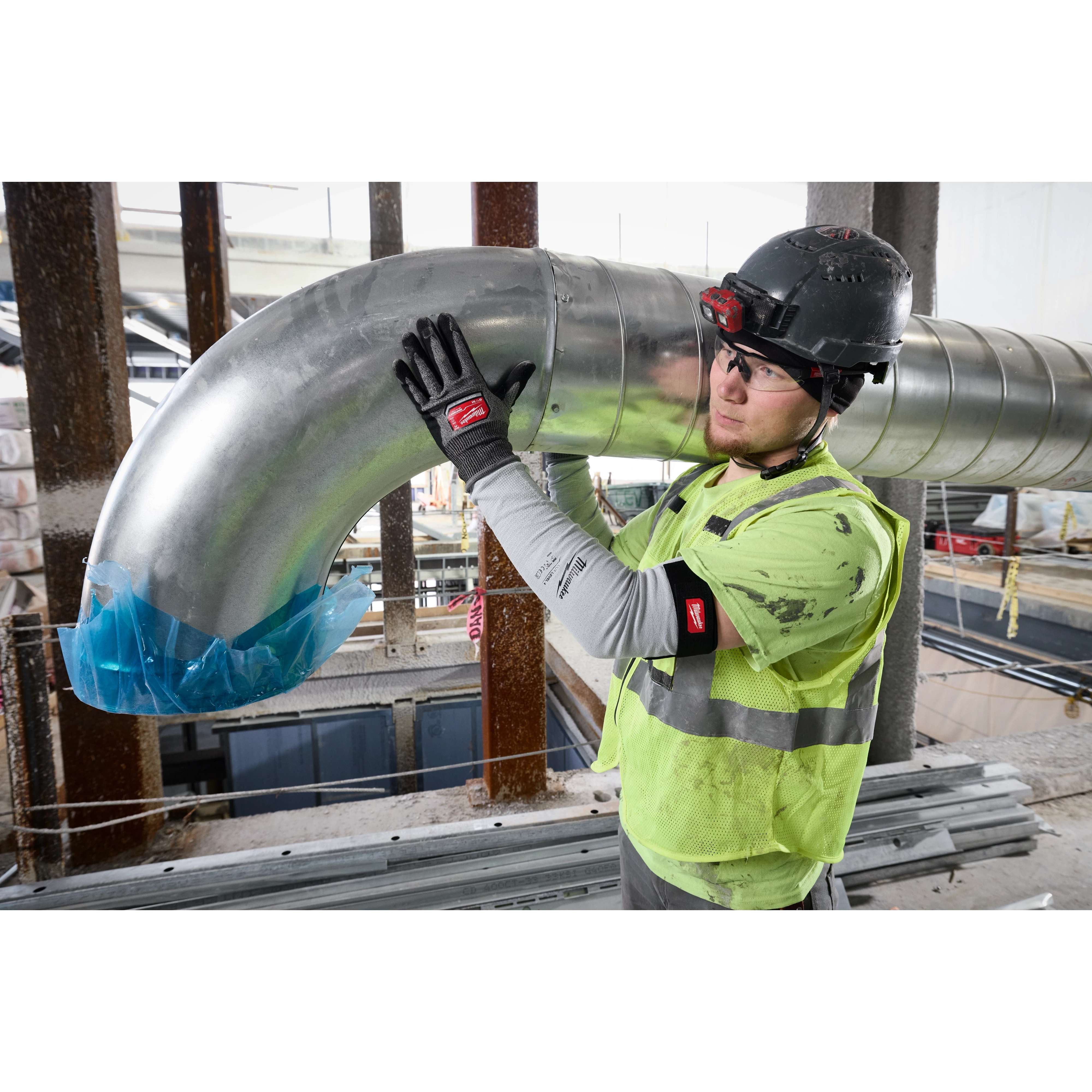 Worker in a construction site wears Cut Level 4 Protective Sleeves, handling a large metal duct in his protective gear.