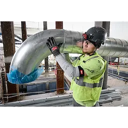 Worker in a construction site wears Cut Level 4 Protective Sleeves, handling a large metal duct in his protective gear.