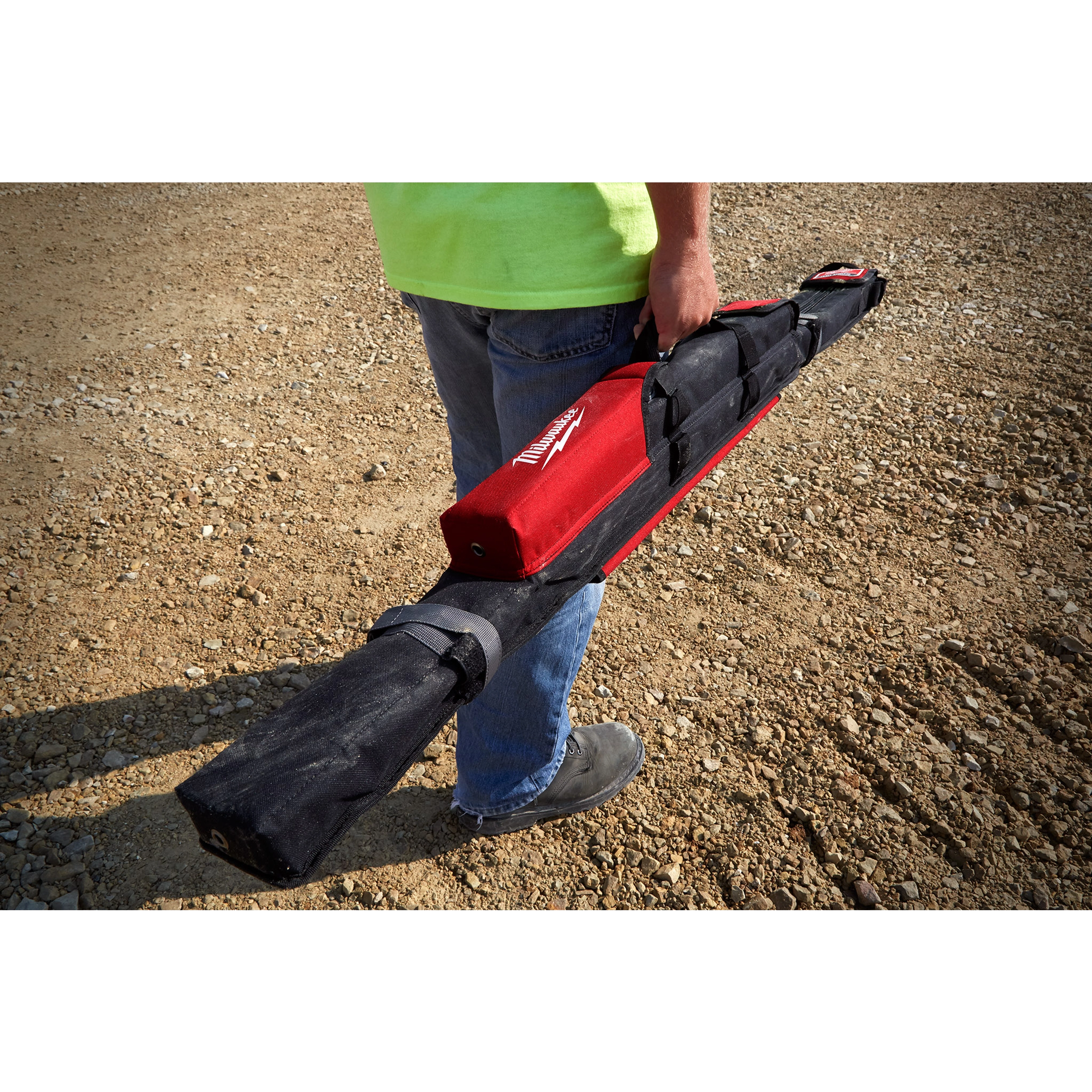 Person carrying the Milwaukee REDSTICK Starter Set in a rugged black and red case on a gravel surface.